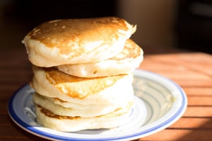 A stack of five fluffy pancakes on a wooden table in direct sunlight