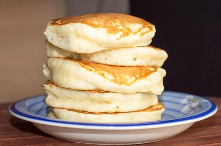 A delicious stack of five extra fluffy pancakes stacked atop a blue plate.