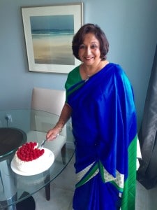 A photo of lemon curd cake being cut by my mother, Chaman Rahim - she is dressed in a vibrant blue and green saree.