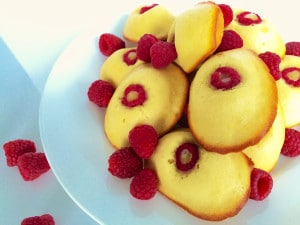 A close-up photo of Lemon-Raspberry madeleines surrounded by a few raspberries