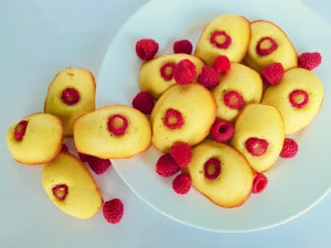 An overhead photo of Lemon-Raspberry Madeleines on, and spilling off, a white plate.