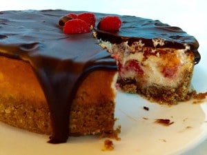 Chocolate-Covered Raspberry Cheesecake with a slice missing, allowing the raspberries within the cake to become visible.