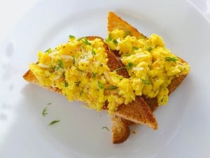 An overhead photo of two slices of toast with scrambled eggs with smoked salmon toppings.