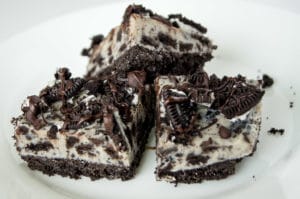Three No Bake Oreo Cheesecake Bars stacked atop one another on a white plate.