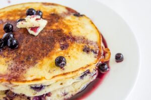 A close-up ¾ angle photo of Blueberry Buttermilk Pancakes topped with blueberry maple syrup and butter.