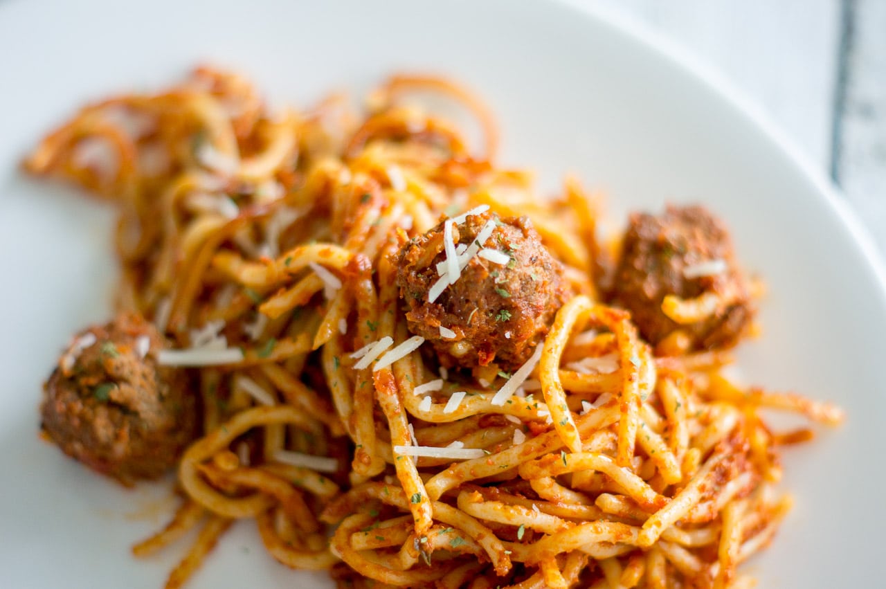 A close-up photo of spaghetti & meatballs with a meatball in the centre.