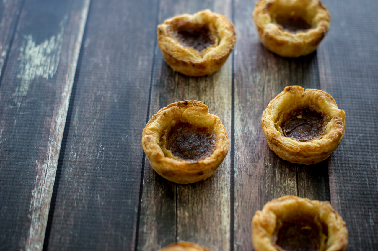 Six Canadian butter tarts in two vertical lines across a dark wood table.
