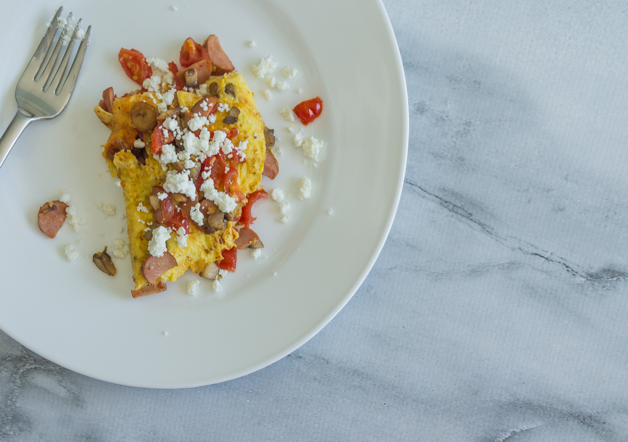 Mushroom omelette topped with chevre and cherry tomatoes on a white plate atop a marble surface.