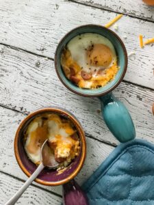 A vertical overhead shot of Cheesy Oeufs en Cocotte / Eggs in Pots, with a spoon cutting into one of the eggs.