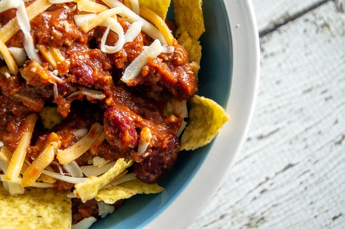 An overhead close-up shot of a bowl of chili con carne with tortilla chips and cheese on top.
