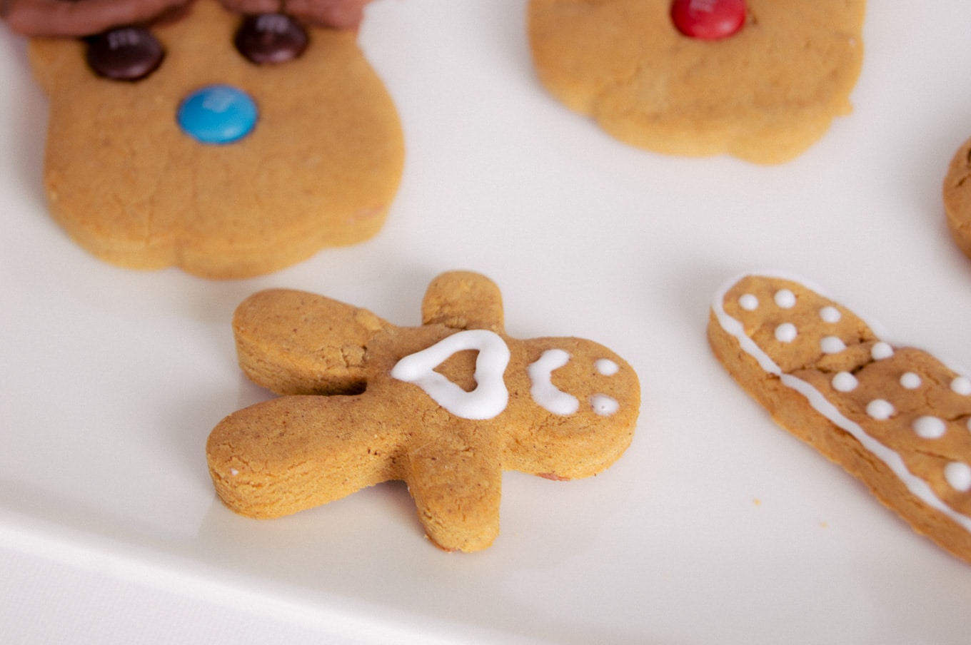 A cute gingerbread man with a smile and a heart on his chest lying between other decorated gingerbread cookies on a white plate.