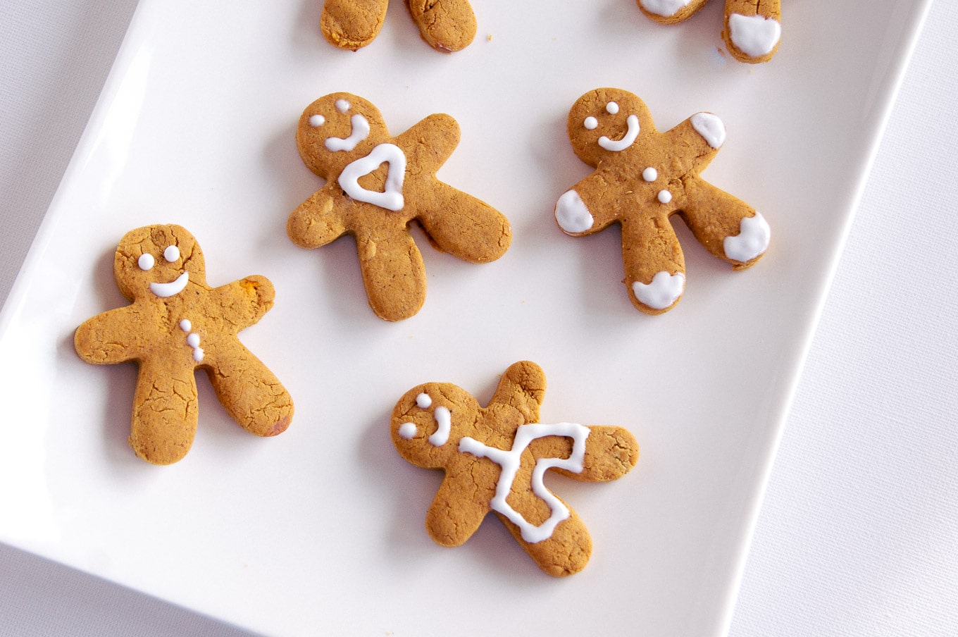 A top-down photo of various gingerbread cookies for Christmas. Each gingerbread man has a different design and facial expression.