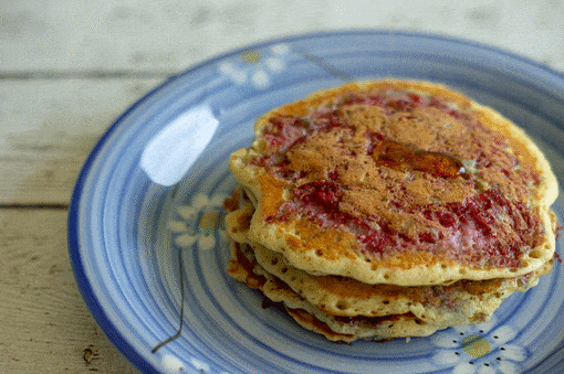 A 5-image gif of maple syrup being drizzled onto a stack Raspberry Swirl Pancakes on a blue plate.