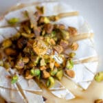 Honey being drizzled on to a baked brie with pistachios piled on top.
