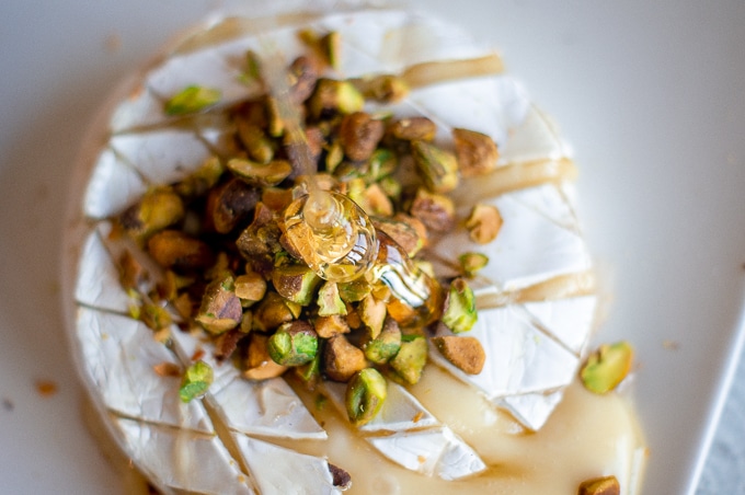 Honey being drizzled on to a baked brie with pistachios piled on top.