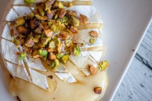 Close-up up of baked brie with honey on crushed pistachios.