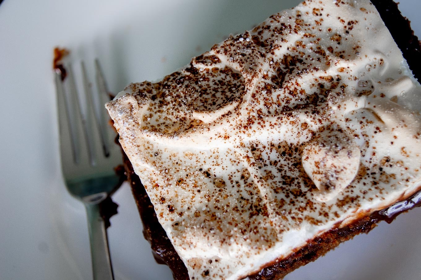 A close-up overhead photo of a slice of gooey chocolate meringue cake, highlighting the deep swirl patterns of the meringue.