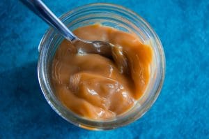 An overhead photo of creamy dulce de leche made using condensed milk centred on a vibrant blue background.