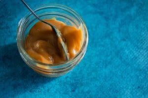 Dulce de leche using condensed milk in a small glass jar on a blue background.