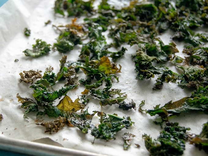 A close-up photo of kale chips that have been baked on parchment paper.