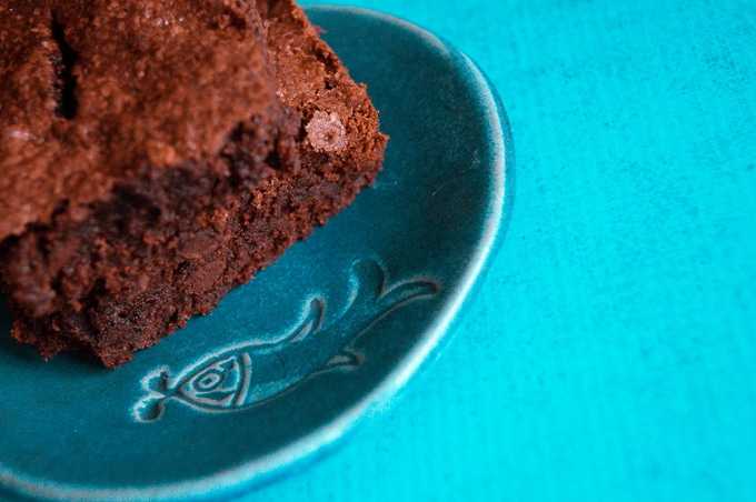 A slightly blurred photo of easy to make olive oil brownies on a green plate with a vibrant blue background.