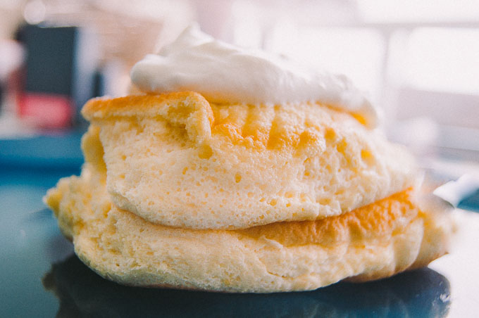 A hero shot of two incredibly fluffy Japanese pancakes with whipped cream on top.