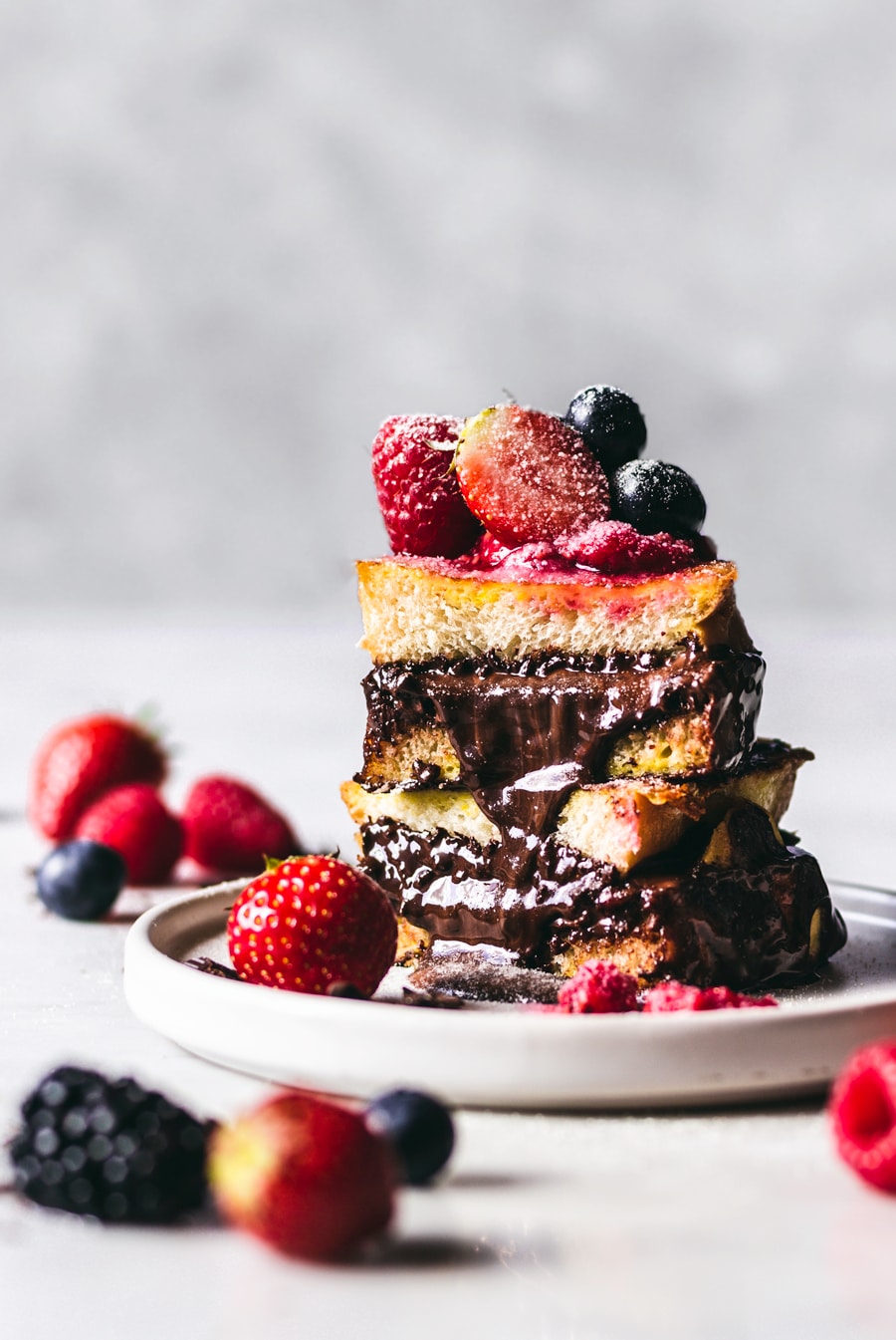 Nutella & Dark Chocolate Stuffed French Toast stacked high on a white plate with the decadent chocolate filling oozing out.