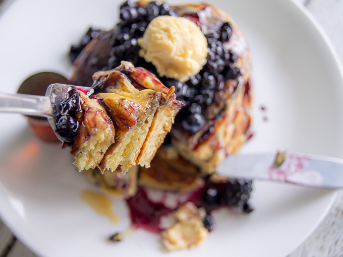 A close-up of blackberry pancakes on a fork with the stack blurred but visible in the background.