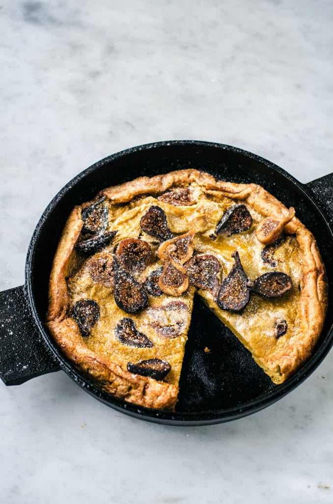 A close-up of the Fig Dutch Baby Pancake in a cast iron pan, with a slice missing.