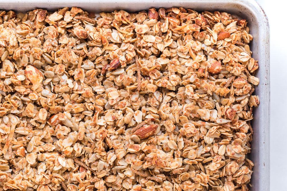Homemade granola right out of the oven in a silver sheet pan.