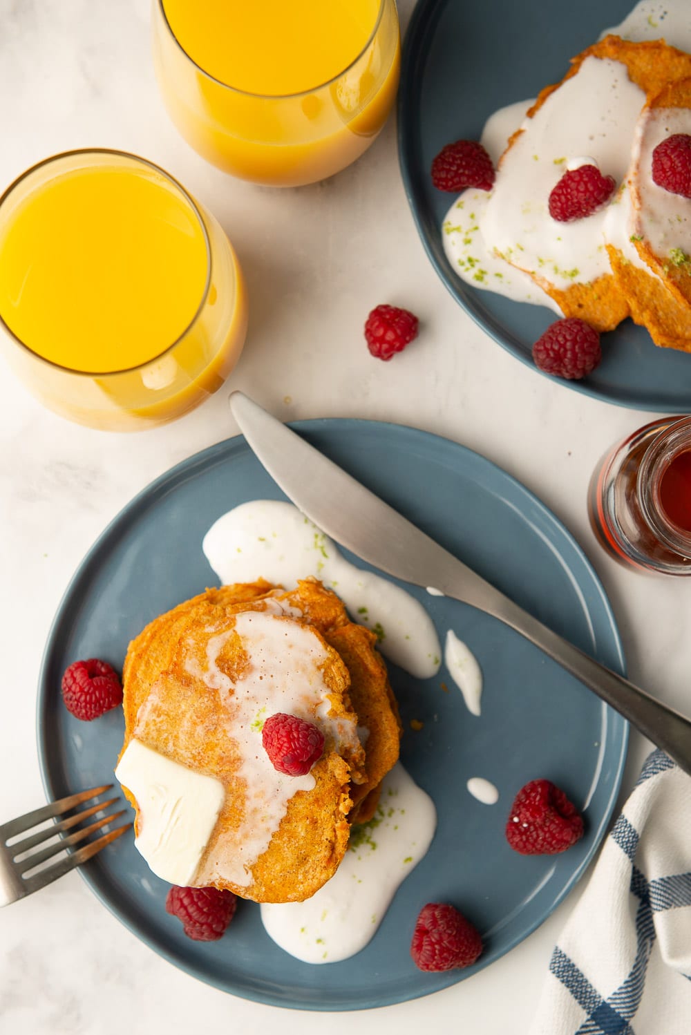 An overhead shot of a plate of healthy sweet potato pancakes topped with coconut whipped cream and raspberries.