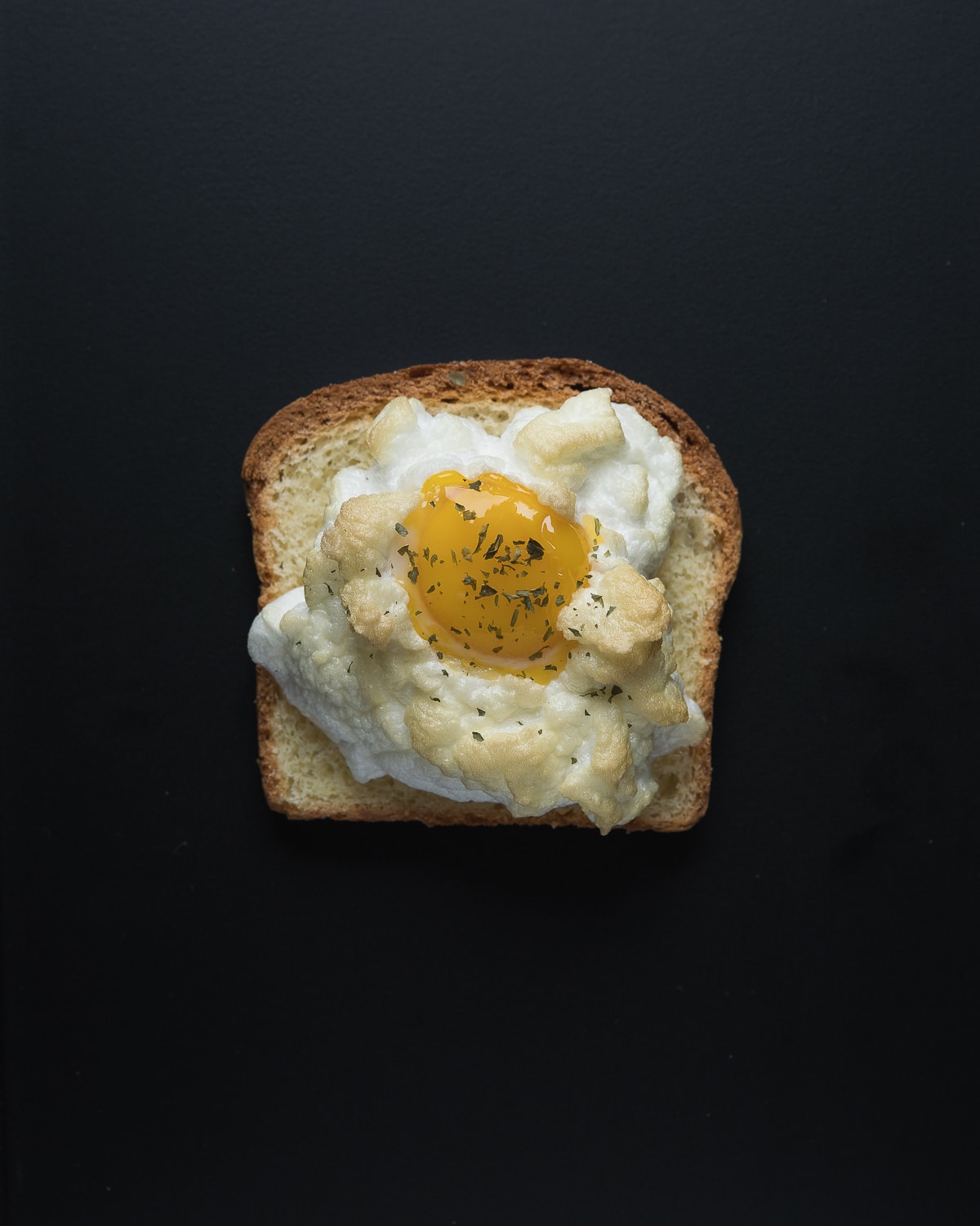 An overhead photo of cloud eggs on toast - the background is entirely black.