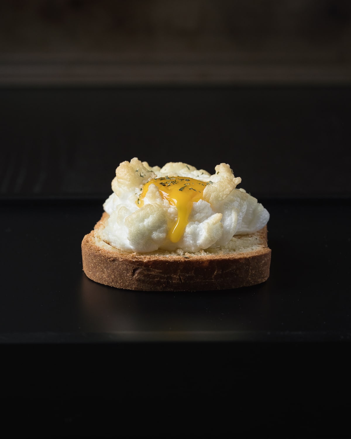 A side view of a cloud egg on toast, the popped yolk is dribbling down the side.