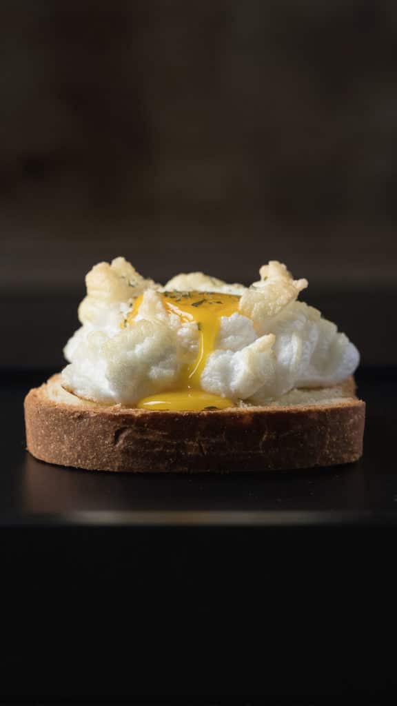 A cloud egg with yolk trailing down the side on to a piece of toast.