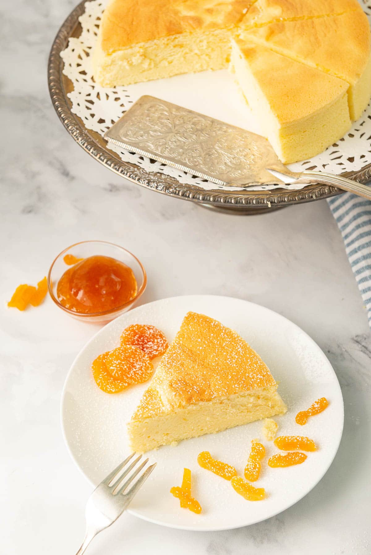 A slice of Japanese cheesecake on a plate, decorated with a little icing sugar, and some pieces of apricot to its side.