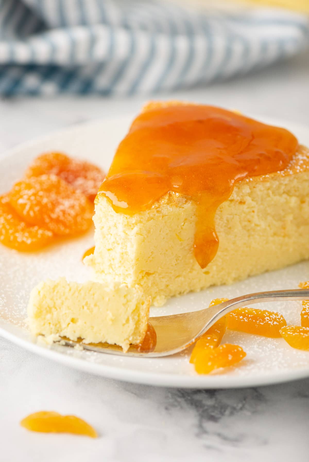 A close-up shot of a slice of cheesecake with apricot glaze trickling down the side.