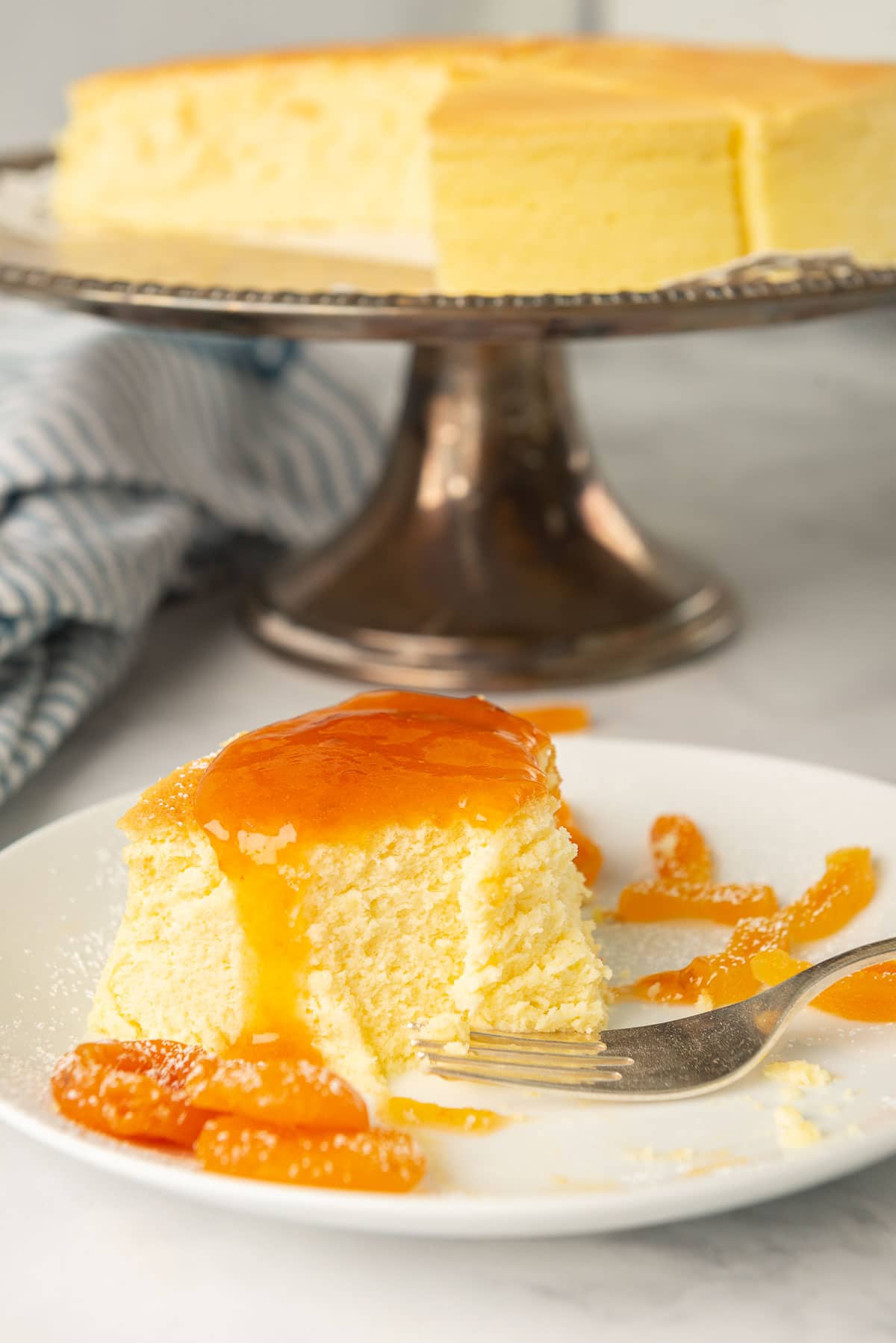A half-eaten slice of Japanese cotton cheesecake that's been glazed with apricot sauce, a bits of sliced apricot.
