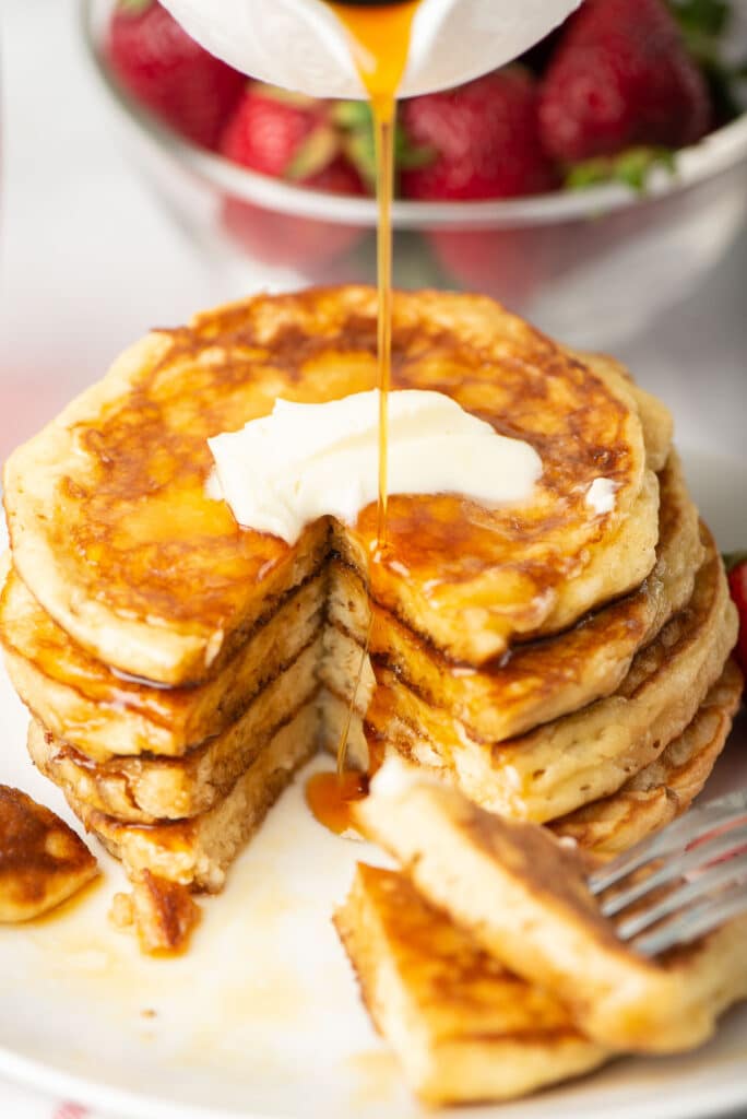 Maple syrup being poured on to a stack of sour cream pancakes.