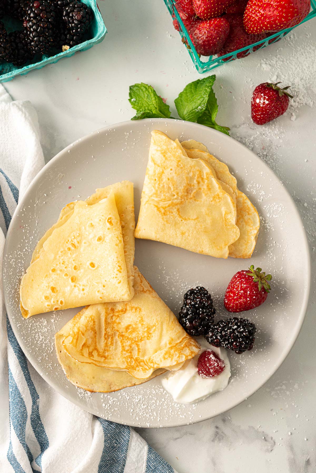 Three crepes folded into triangles with berries and whipped cream on the side.