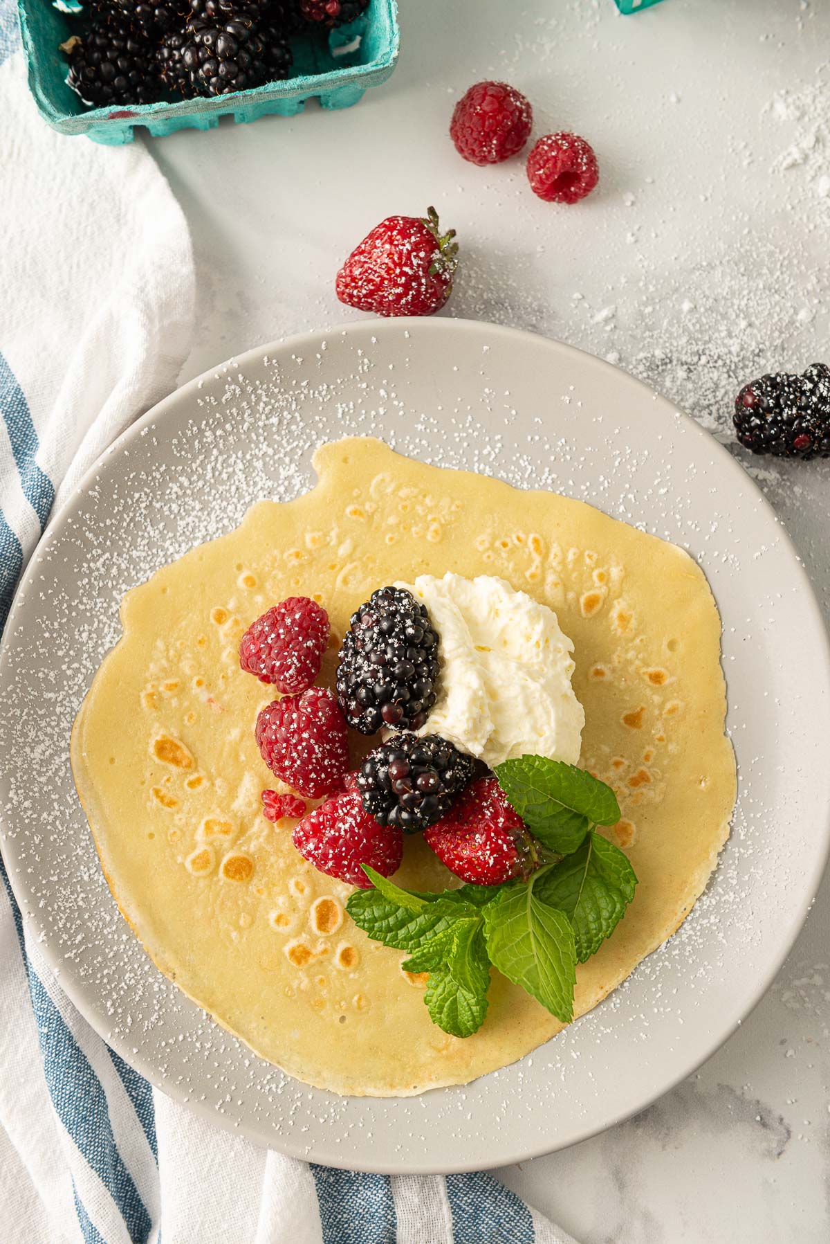 An unfolded crepe that's been filled with raspberries, blackberries, whipped cream, and a sprinkle of icing sugar.