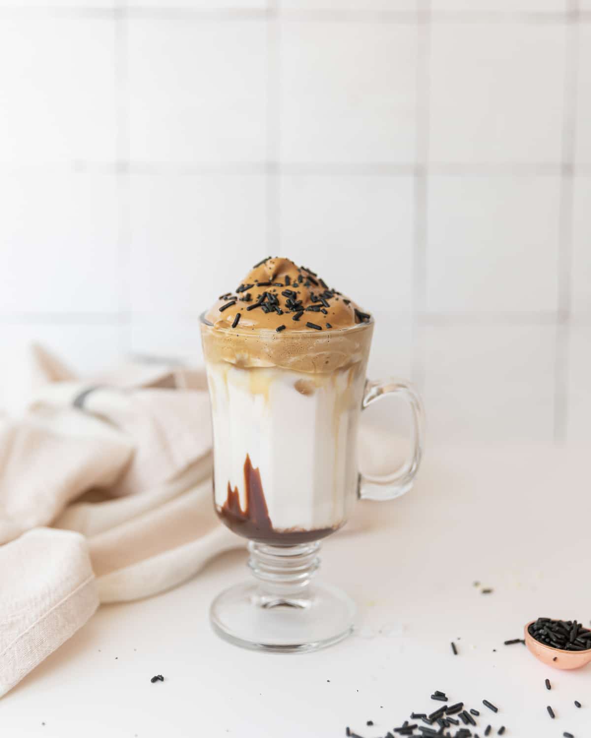 A side on view of a completed cup of mocha dalgona coffee with chocolate sprinkles on top.