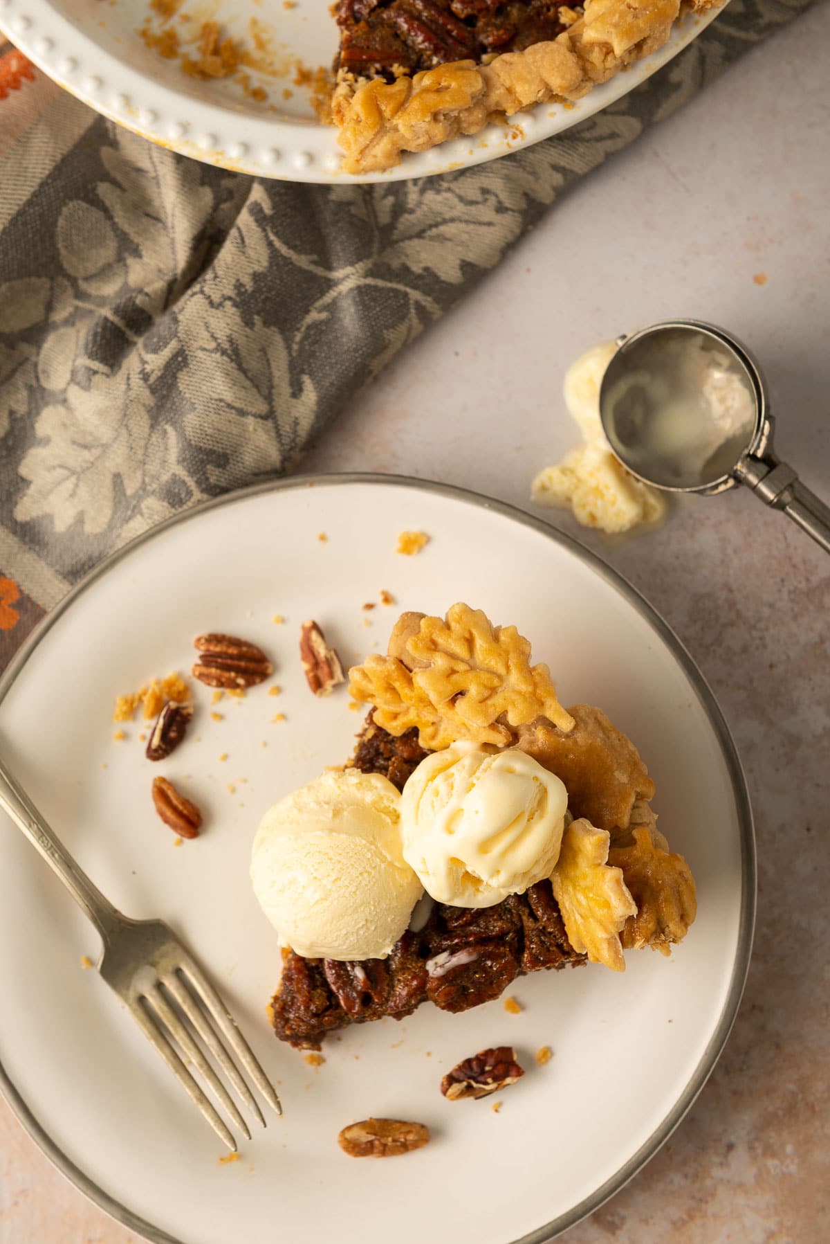 Flatlay of a slice of pecan pie with two scoops of vanilla ice cream on top.