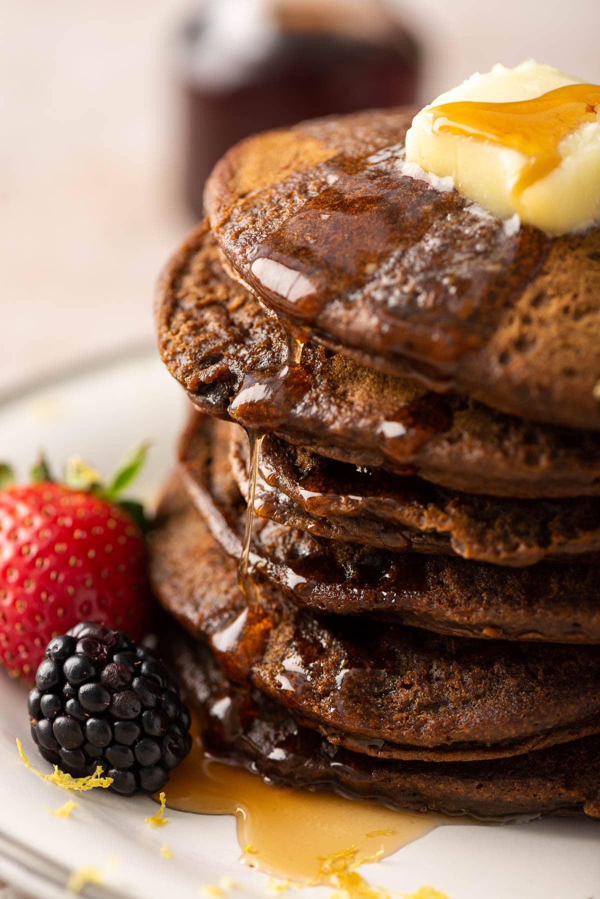 A close-up view of the side of a stack of gingerbread pancakes with maple syrup trickling down the sides.