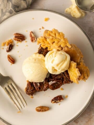 A slice of pecan pie on a white plate with two scoops of vanilla ice cream.