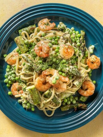 Blue plate full of roasted shrimp & asparagus linguine on a pale yellow background.