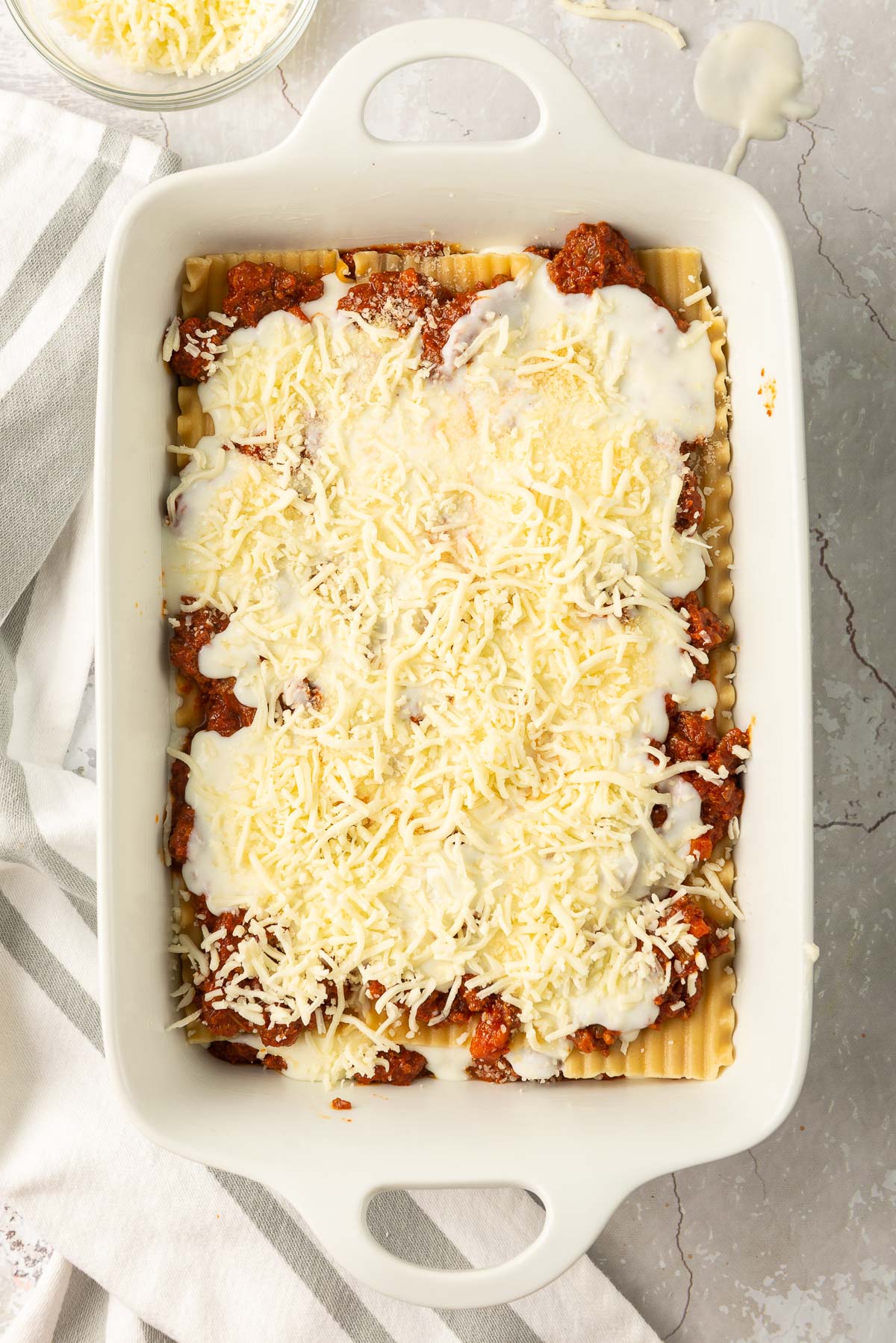 An uncooked lasagne alla bolognese in a white baking dish.