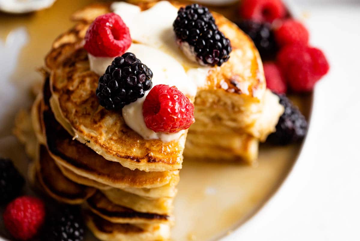 A close-up overhead photo of yogurt pancakes, with bright berries, a dollop of Greek yogurt, and some maple syrup on top.