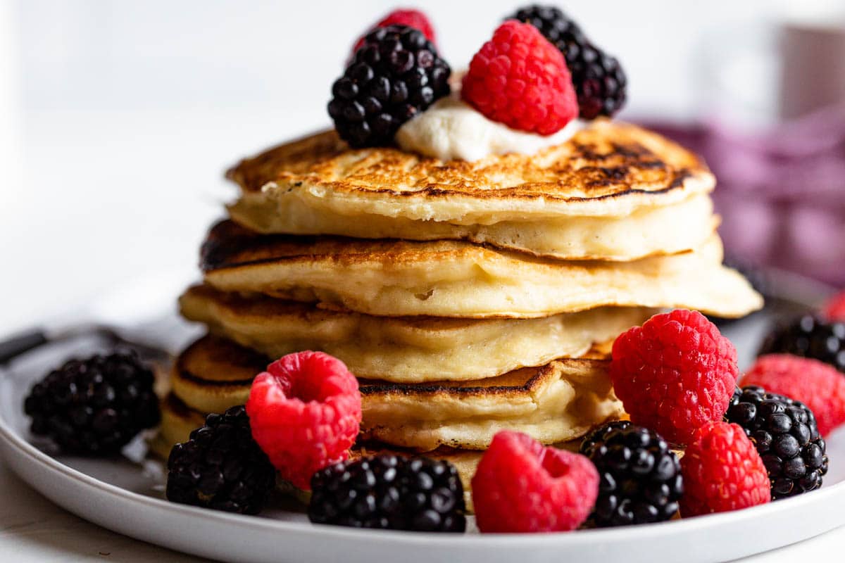 A stack of fluffy Greek yoghurt pancakes decorated with plenty of raspberries and blackberries.