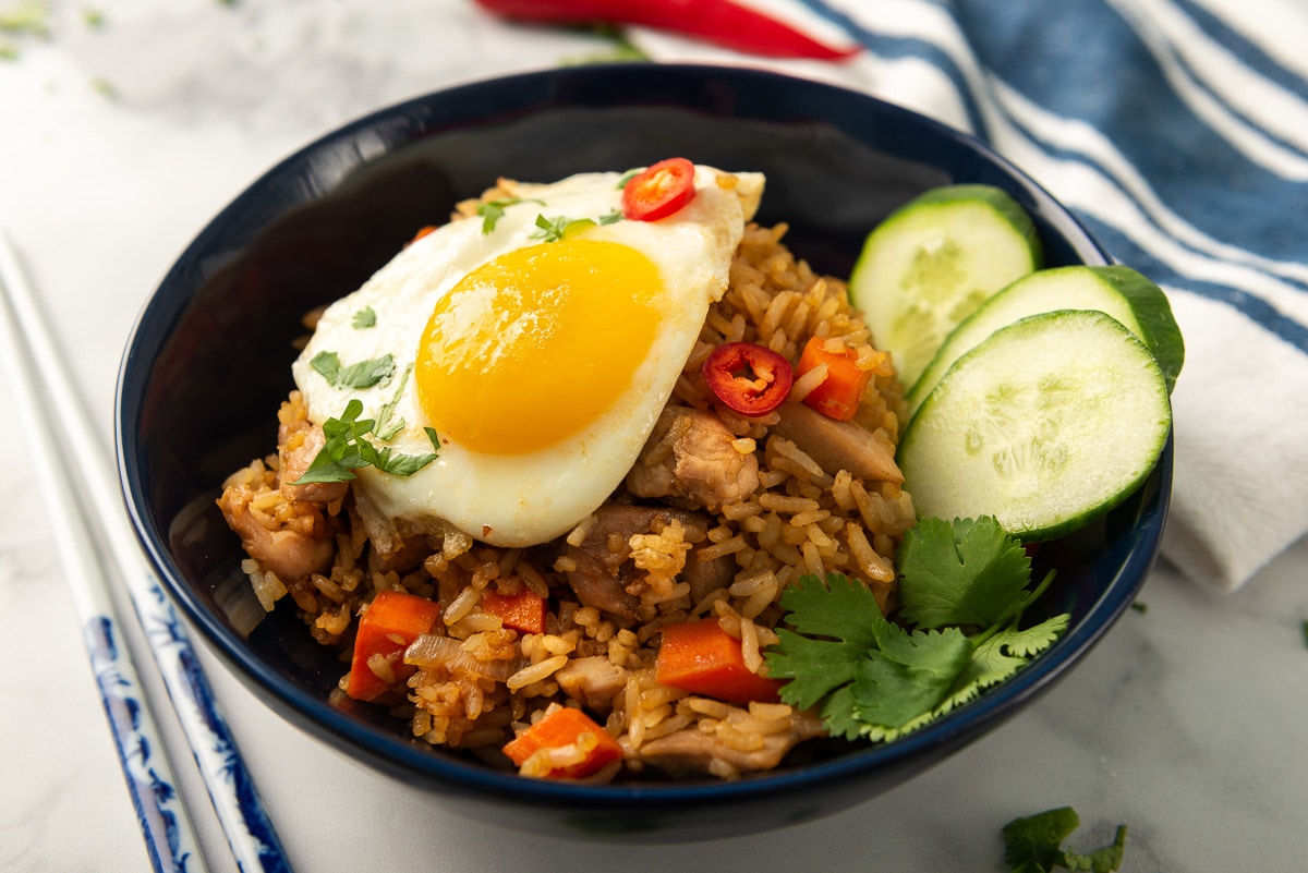 A close up photo of nasi goreng with an egg on top, garnished with some cucumbers.