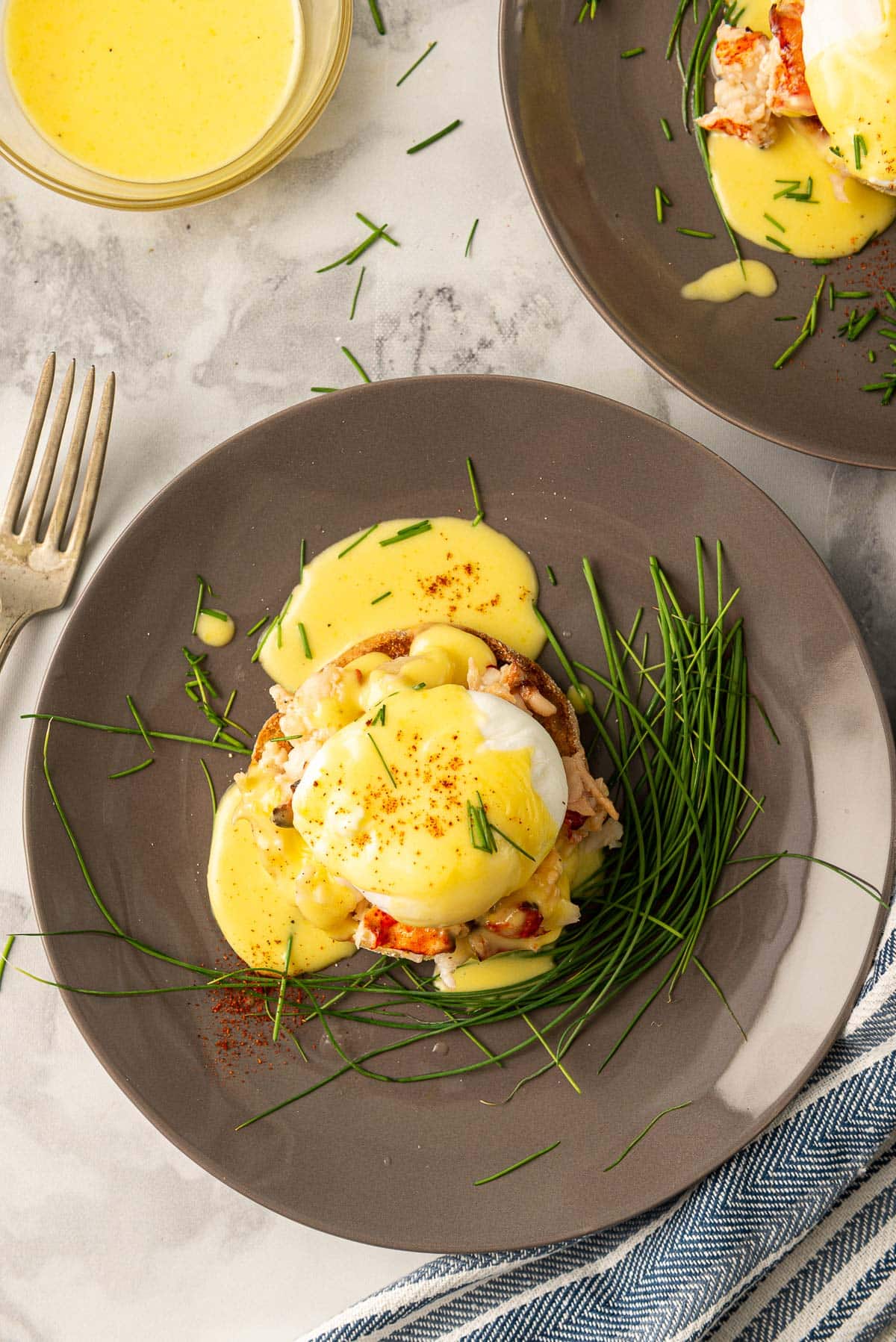 Lobster eggs benedict on a dark plate with hollandaise on top.